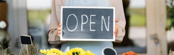 Partial view holding board with open lettering near flowers on foreground, banner — Stock Photo