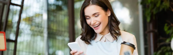 Alegre florista sosteniendo café para llevar y mensajería en el teléfono inteligente durante el freno, pancarta - foto de stock