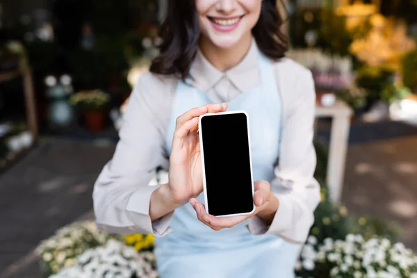 Vista cortada de florista sorridente segurando smartphone com tela em branco perto de flores em primeiro plano borrado — Fotografia de Stock