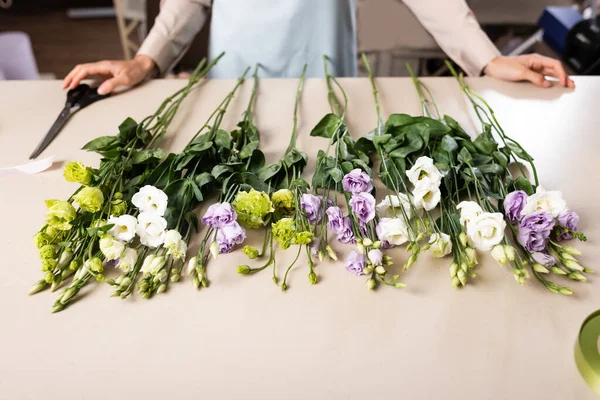 Vista ritagliata di fiorista vicino eustoma fiori sul tavolo in negozio di fiori su sfondo sfocato — Foto stock