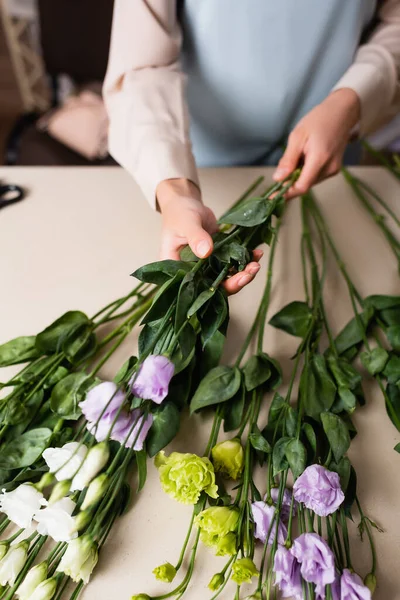 Vista parziale del fiorista che tiene fiori di eustoma mentre organizza bouquet su sfondo sfocato — Foto stock