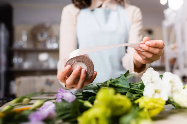 Cropped view of florist holding decorative ribbon near eustoma flowers while making bouquet on blurred foreground — Stock Photo