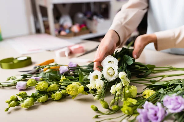 Partial view of florist making eustoma flowers bouquet in flower shop on blurred foreground — Stock Photo