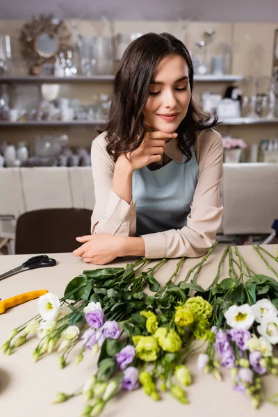 Floristería feliz mirando flores eustoma en la mesa en la tienda de flores en primer plano borrosa - foto de stock