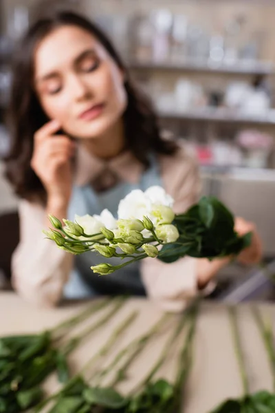 Jeune fleuriste tenant des fleurs d'eustomie sur fond flou — Photo de stock