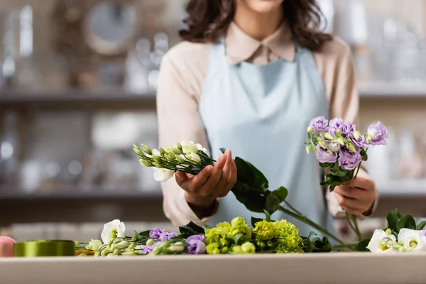 Vista parcial de florista sosteniendo flores de eustoma mientras hace ramo en la tienda de flores en primer plano borroso - foto de stock