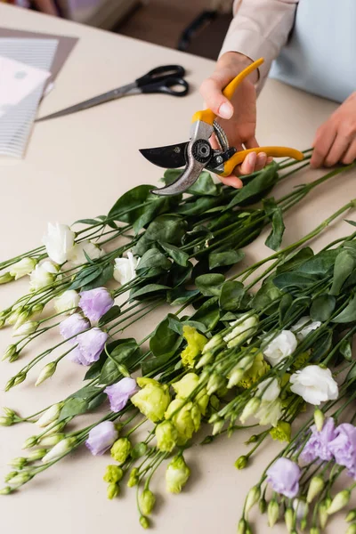 Cropped view of florist holding secateurs while making bouquet with eustoma flowers — Stock Photo