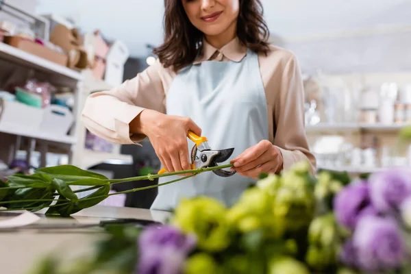 Partial view of cheerful florist cutting steam near flowers of blurred foreground — Stock Photo