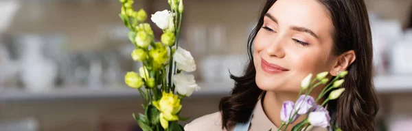 Florista joven sonriendo mientras mira flores eustoma, pancarta - foto de stock