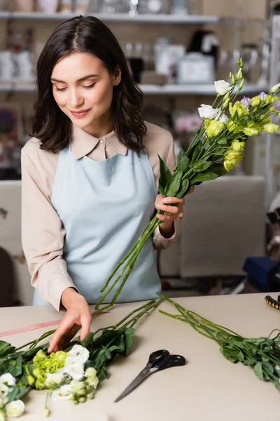 Fiorista giovane che tiene fiori di eustoma mentre fa mazzo in negozio di fiori — Foto stock