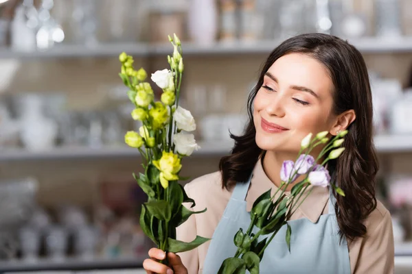 Fröhlicher Blumenhändler hält Eustoma-Blumen in Blumenladen auf verschwommenem Hintergrund — Stockfoto