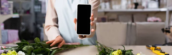Vista cortada de florista mostrando smartphone com tela em branco perto da mesa com flores eustoma no fundo borrado, banner — Fotografia de Stock
