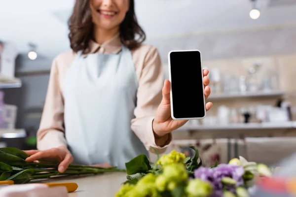Обрезанный вид флориста показывающий смартфон с чистым экраном рядом с цветами эустомы на столе на размытом фоне — стоковое фото