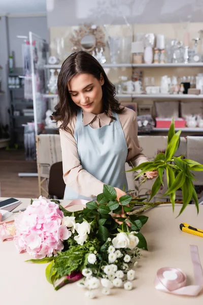 Florista sonriente componiendo ramo con hortensias, crisantemos y rosas con bastidores borrosos sobre fondo - foto de stock