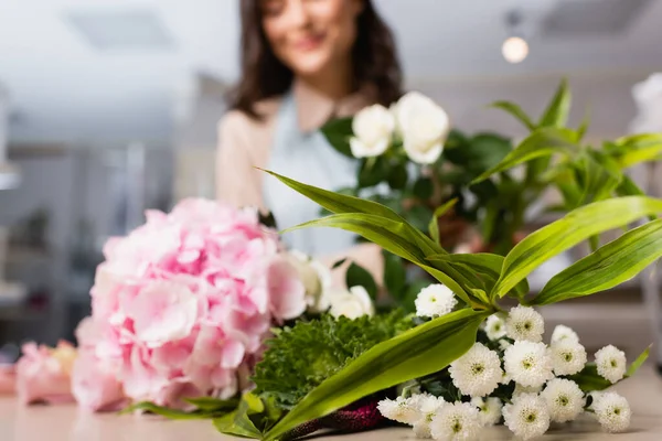 Close up view chrysanthemums and hydrangea on desk with blurred female florist on background — Stock Photo