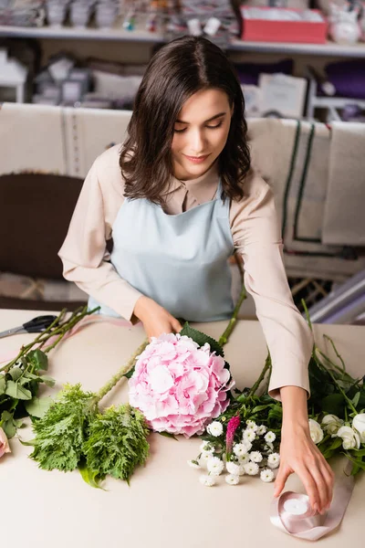 Hochwinkel-Ansicht des Floristen unter dekorativen Band vom Schreibtisch in der Nähe von Blumen auf verschwommenem Hintergrund — Stockfoto