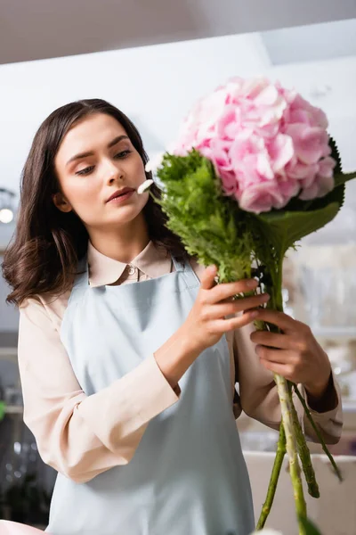 Focused female florist composing bouquet with blooming hydrangea in flower shop on blurred foreground — Stock Photo