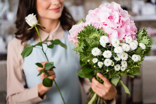 Vista recortada de florista femenina con ramo de rosas componiendo con hortensias y crisantemos sobre fondo borroso - foto de stock