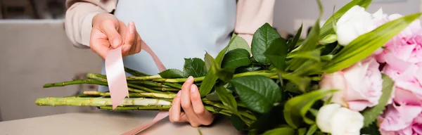 Cropped view of florist with decorative ribbon tying stalks of bouquet on table, banner — Stock Photo