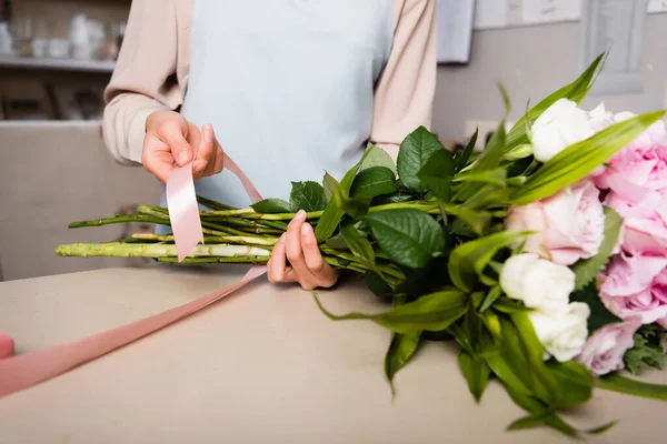 Vista ritagliata di fiorista femminile con nastri decorativi steli di bouquet fresco in negozio di fiori su sfondo sfocato — Foto stock