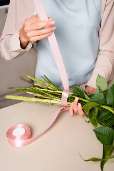 Cropped view of female florist with decorative ribbon tying stalks of bouquet on desk — Stock Photo