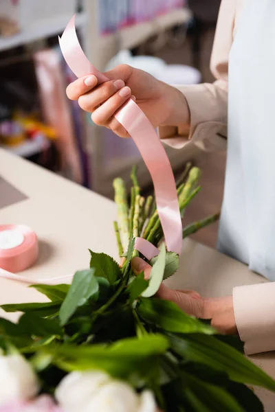 Close up view of florist hand holding decorative ribbon, while tying stalks of bouquet in flower shop on blurred background — Stock Photo