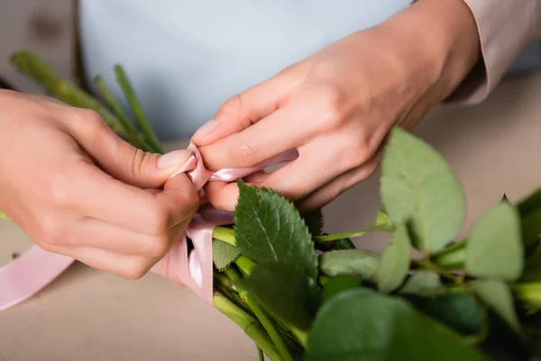 Vista de cerca de las manos floristas atando tallos de ramo con cinta decorativa sobre fondo borroso - foto de stock