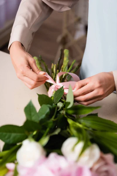 Cropped view of florist tying bow on bouquet stalks on blurred foreground — Stock Photo