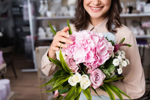Vue recadrée de fleuriste femelle touchant hortensia floraison, tout en tenant bouquet avec des rayonnages flous sur le fond — Photo de stock