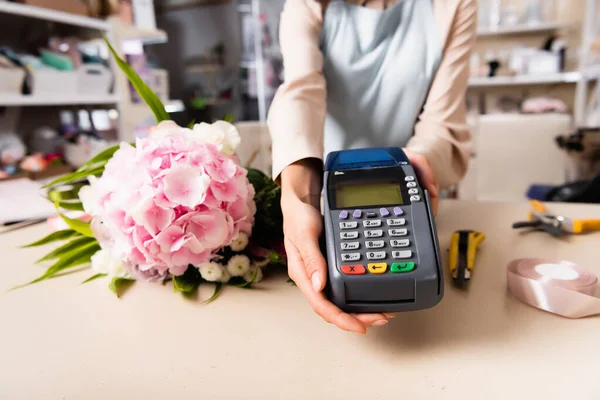 Cropped view of florist holding terminal near fresh bouquet on desk on blurred background — Stock Photo