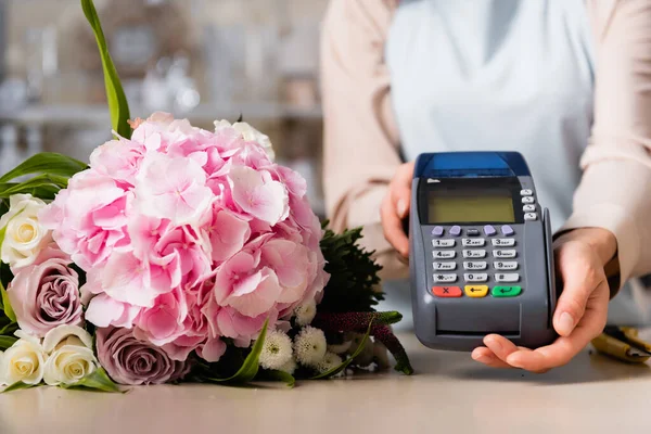 Nahaufnahme des Terminals in den Händen des Blumenhändlers in der Nähe von frischem Strauß auf dem Schreibtisch auf verschwommenem Hintergrund — Stockfoto