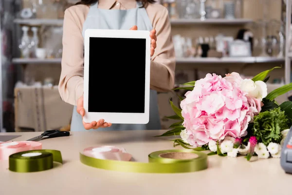 Vista recortada de floristería mostrando tableta digital con pantalla en blanco cerca del ramo en el escritorio sobre fondo borroso - foto de stock