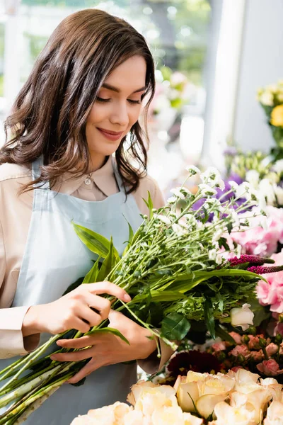 Lächelnde Floristin mit einem Strauß Chrysanthemen und Celosia mit verschwommenen Blumen auf dem Hintergrund — Stockfoto