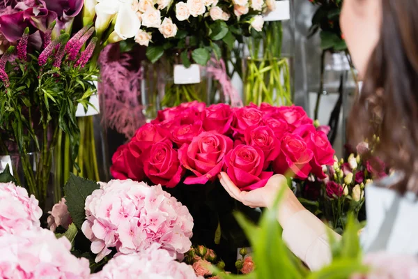 Vista cortada de florista feminino cuidando de rosas em prateleiras de flores em primeiro plano borrado — Fotografia de Stock