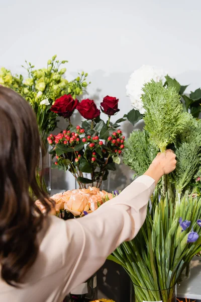 Rückansicht einer Floristin, die grüne Pflanze aus der Vase auf einem Blumengestell im unscharfen Vordergrund nimmt — Stockfoto