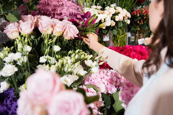 Cropped view of female florist taking celosia from vase on flower rack with blurred roses on foreground — Stock Photo
