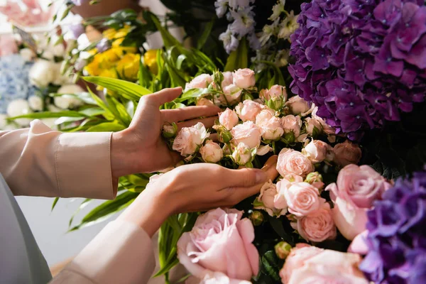Cropped view of female florist caring about roses near purple hydrangeas on blurred background — Stock Photo