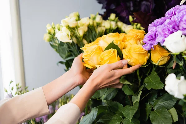 Vista cortada de florista feminino cuidando de rosas amarelas perto da variedade de flores no fundo borrado — Fotografia de Stock