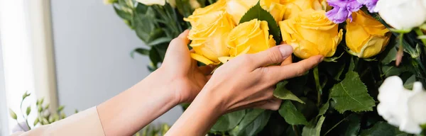 Vista ritagliata del fiorista femminile che si prende cura delle rose gialle vicino ai fiori in negozio, banner — Foto stock