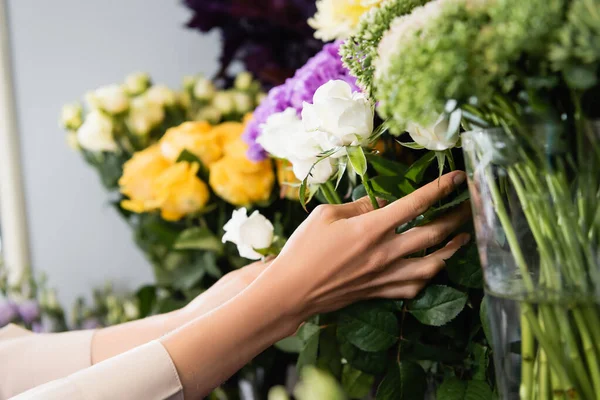 Ausgeschnittene Ansicht einer Floristin, die sich um weiße Rosen auf einem Blumenständer im Geschäft auf verschwommenem Hintergrund kümmert — Stockfoto