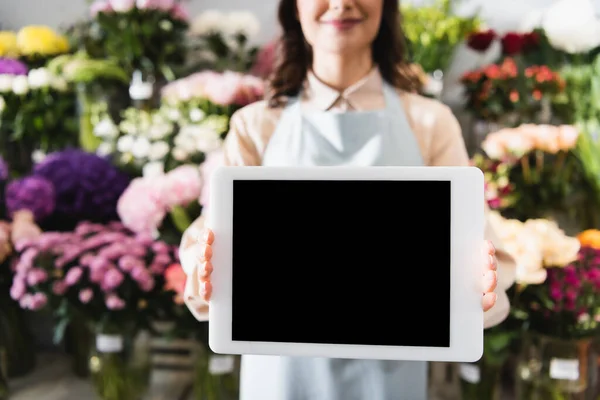 Vista cortada de florista feminino mostrando tablet digital com tela em branco com gama turva de flores no fundo — Fotografia de Stock