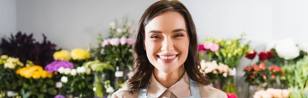 Portrait de fleuriste heureux regardant la caméra avec une gamme floue de fleurs sur fond, bannière — Photo de stock