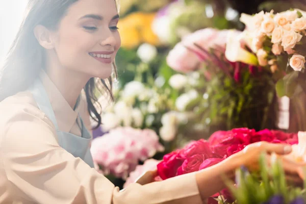 Щасливий жіночий флорист піклується про квіти на розмитому фоні — стокове фото