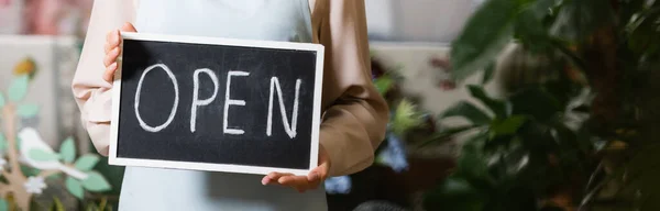 Vista recortada de florista femenina sosteniendo pizarra con letras abiertas sobre fondo borroso, pancarta - foto de stock