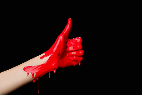 Vista recortada de la mano pintada en pintura roja que muestra el pulgar hacia arriba aislado en negro - foto de stock