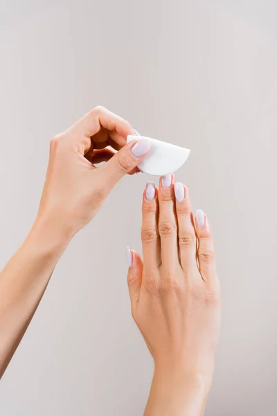 Cropped view of woman cleaning fingernails with cotton pad isolated on grey — Stock Photo