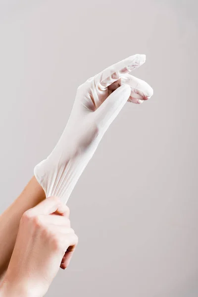 Обрезанный вид женщины, надевающей латексную перчатку, изолированную от серого — стоковое фото