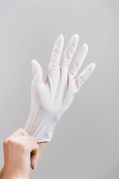 Cropped view of woman putting on latex glove isolated on grey — Stock Photo