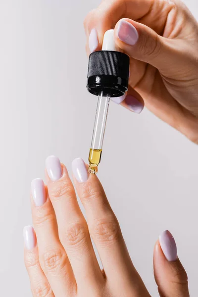 Vista recortada de la mujer aplicando aceite de pipeta en las uñas aisladas en gris - foto de stock