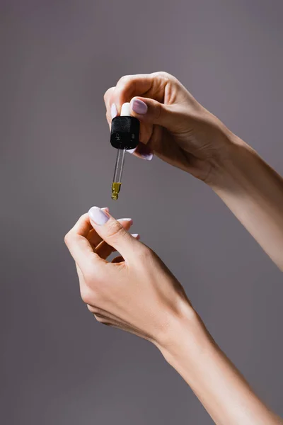 Обрізаний вид жінки, що наносить олію з піпетки на нігті ізольовані на сірому — стокове фото